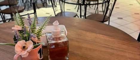 A round wooden table with a pink flower vase and a clear glass container with a pink lid.