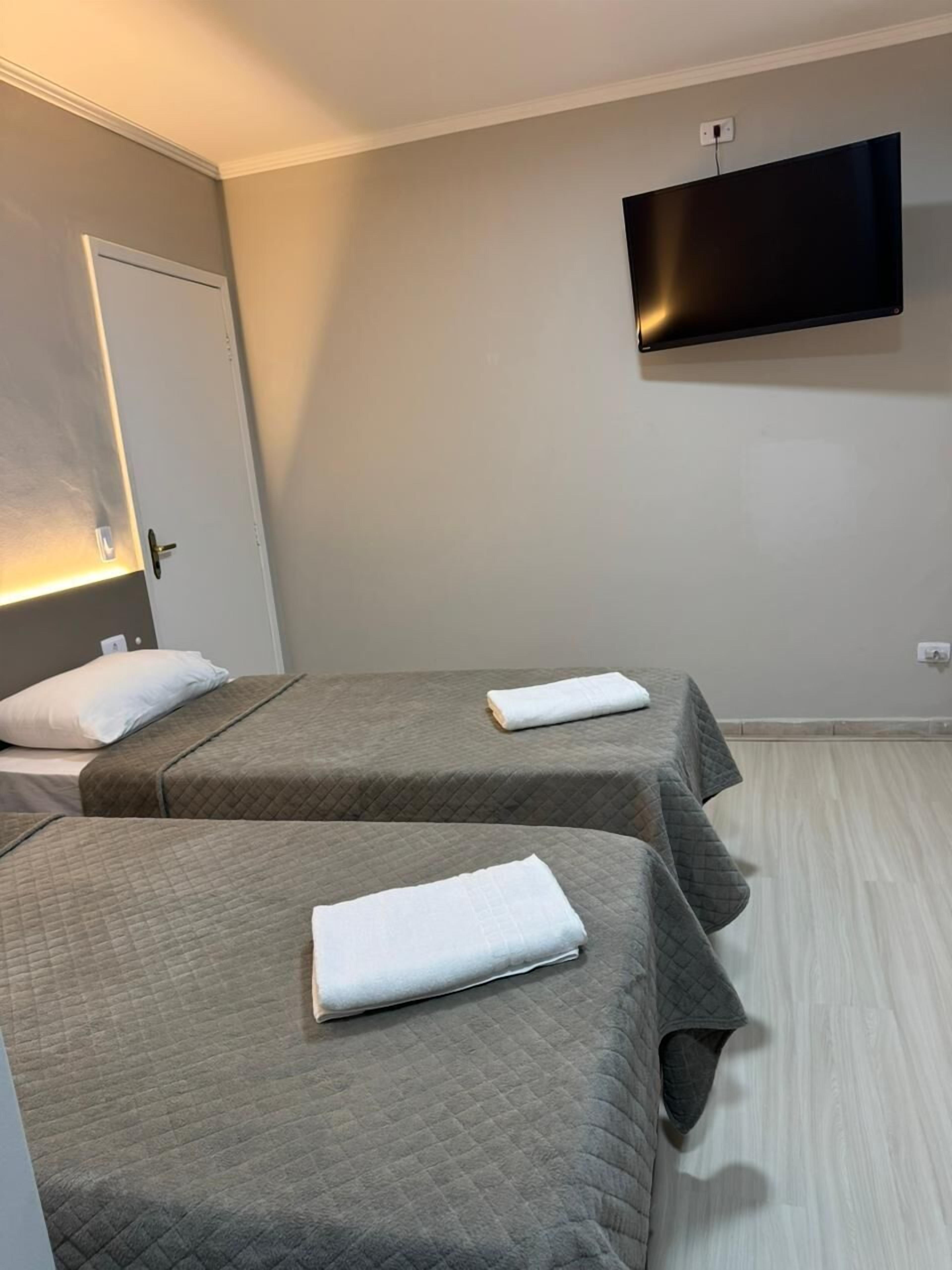 A hotel room with two beds, a flat-screen TV mounted on the wall, and a door with a light above it.