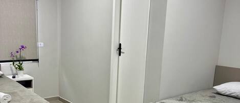 Una habitación de hotel con dos camas, una mesita con un jarrón de flores y una puerta.