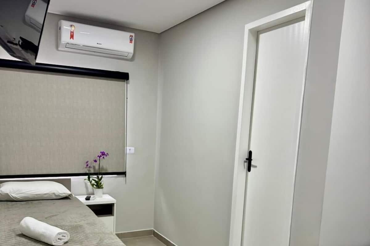 Una habitación de hotel con cama, una silla, un escritorio, una mesita con una planta y una puerta.