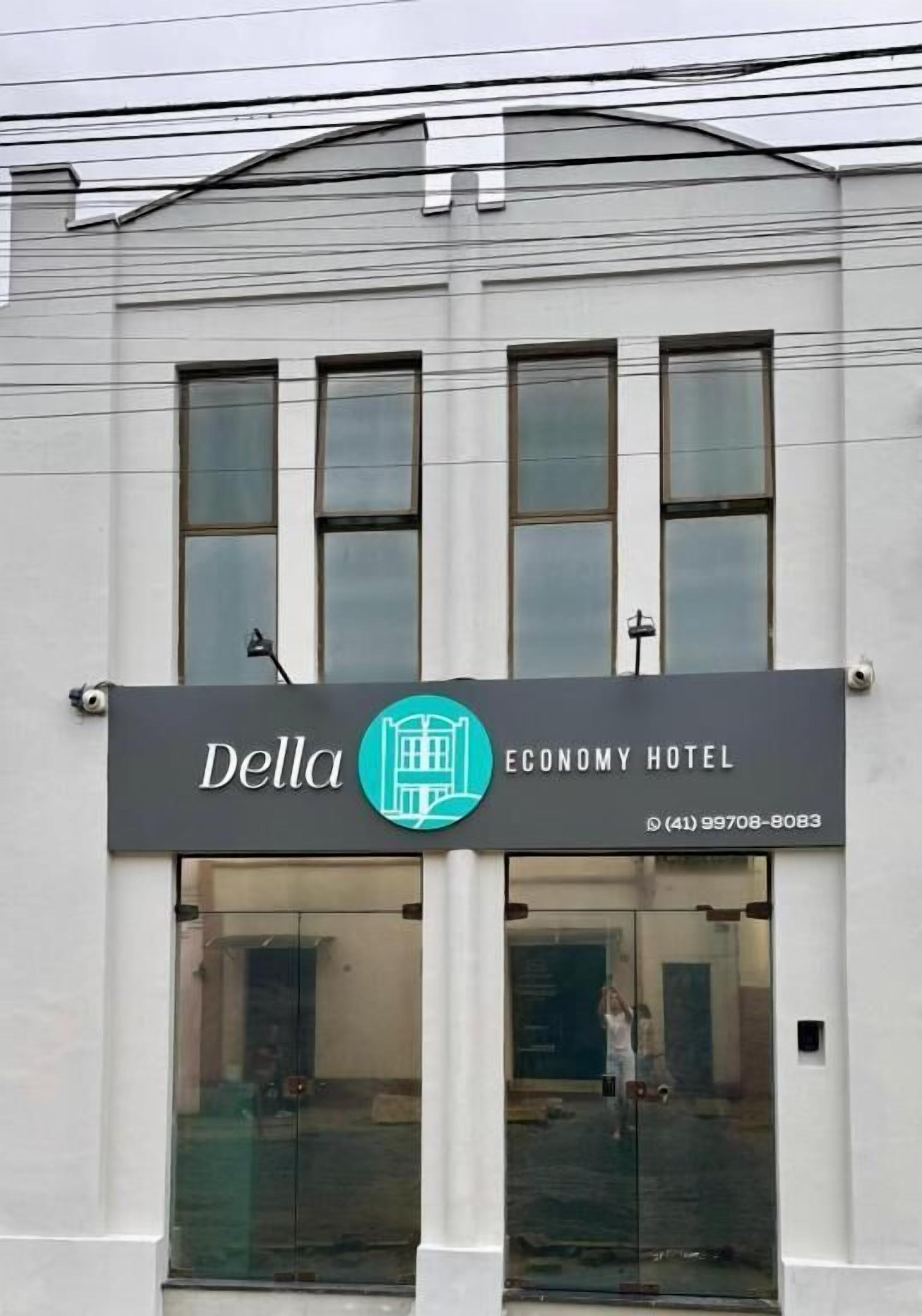 The exterior of the Della Economy Hotel with a large glass entrance and a sign displaying the hotel's name and contact number.