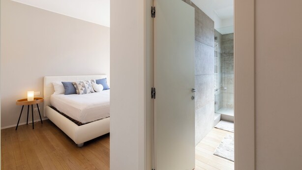 A bedroom with a bed, bedside table, and a door leading to a shower area. - notaMI - HELLO Navigli (Milan)