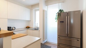 A modern kitchen with white cabinets, a stainless steel refrigerator, a wooden countertop, and a window with a plant. - notaMI - HELLO Navigli (Milan)