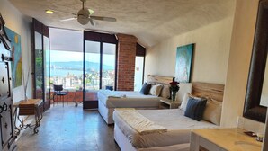 Habitación de hotel con dos camas, un balcón con vistas a la ciudad, ventilador de techo y un ventanal grande.
