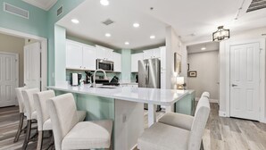 A modern kitchen with white cabinets, a stainless steel refrigerator, and a central island with bar stools. - Condo with Walking Distance To Pool (Kissimmee)