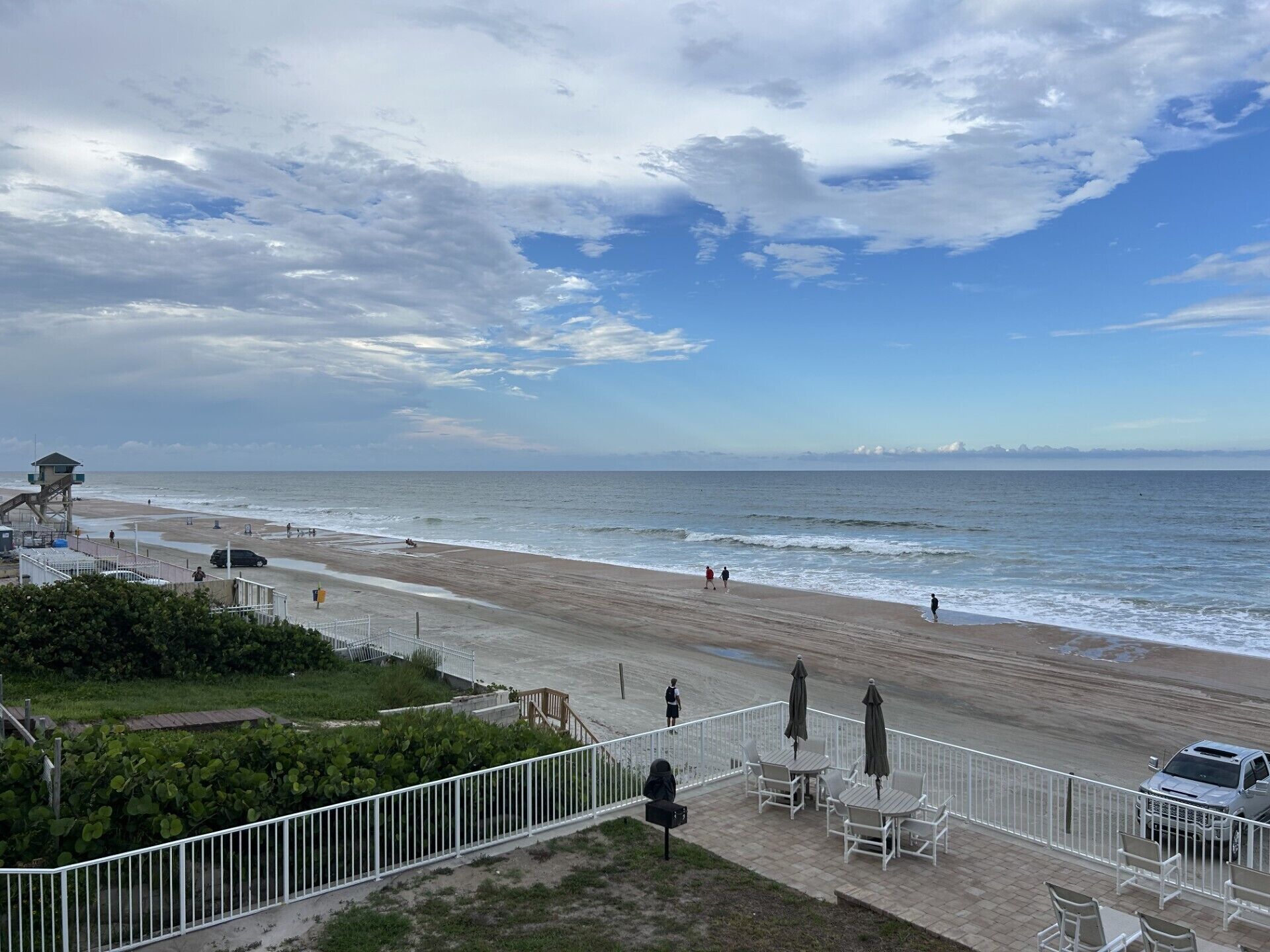 Ein Strand mit einem Rettungsturm, einem eingezäunten Weg und Liegestühlen.