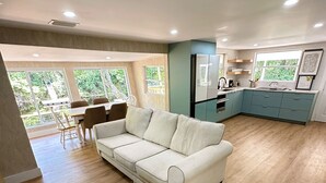 Amplia sala de estar con un sofá blanco, piso de madera y una cocina con armarios color turquesa.