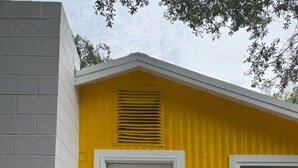 Un pequeño edificio amarillo con puerta y ventana blancas, y un porche con barandilla blanca y felpudo negro.