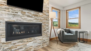 Una sala de estar moderna con chimenea de piedra, televisor de pantalla plana, sofá de cuero y vistas al exterior a través de amplios ventanales.