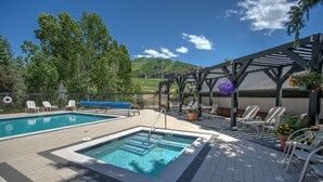 Zona de piscina con dos piscinas, sillas de descanso y una pérgola adornada con flores.