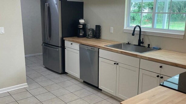 A modern kitchen with a stainless steel refrigerator, a dishwasher, a coffee maker, and a window providing a view of the outdoors. - Spacious 4 Bedroom Retreat Near Lake & Charleston (Moncks Corner)