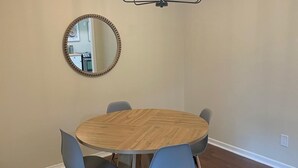 A dining area with a round wooden table, four blue chairs, a mirror, and a modern chandelier. - Spacious 4 Bedroom Retreat Near Lake & Charleston (Moncks Corner)