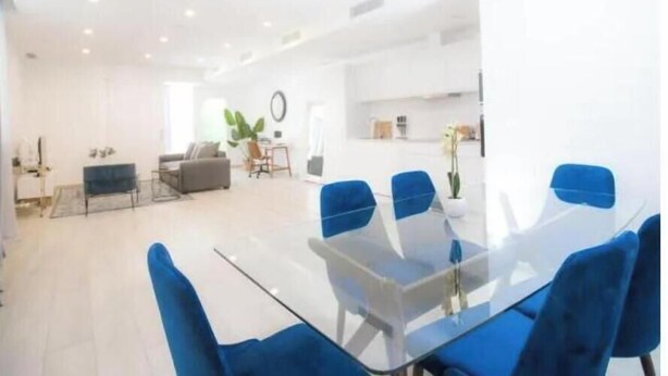 Una sala de estar moderna con una mesa de comedor de cristal y sillas azules, un sofá gris y una mesa de centro.