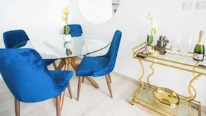 Un coin repas avec une table ronde, des chaises bleues, une table d’appoint à cadre doré avec un plateau en verre et un miroir au mur.