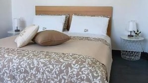 Ein ordentlich bezogenes Bett mit einem gemusterten Überwurf, zwei Kissen und einem Kopfteil. Zwei Nachttische mit Lampen und einem kleinen dekorativen Gegenstand sind vorhanden.