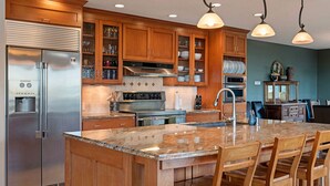 Una cucina con mobili in legno, frigorifero in acciaio inox, isola con sgabelli da bar e illuminazione a sospensione.