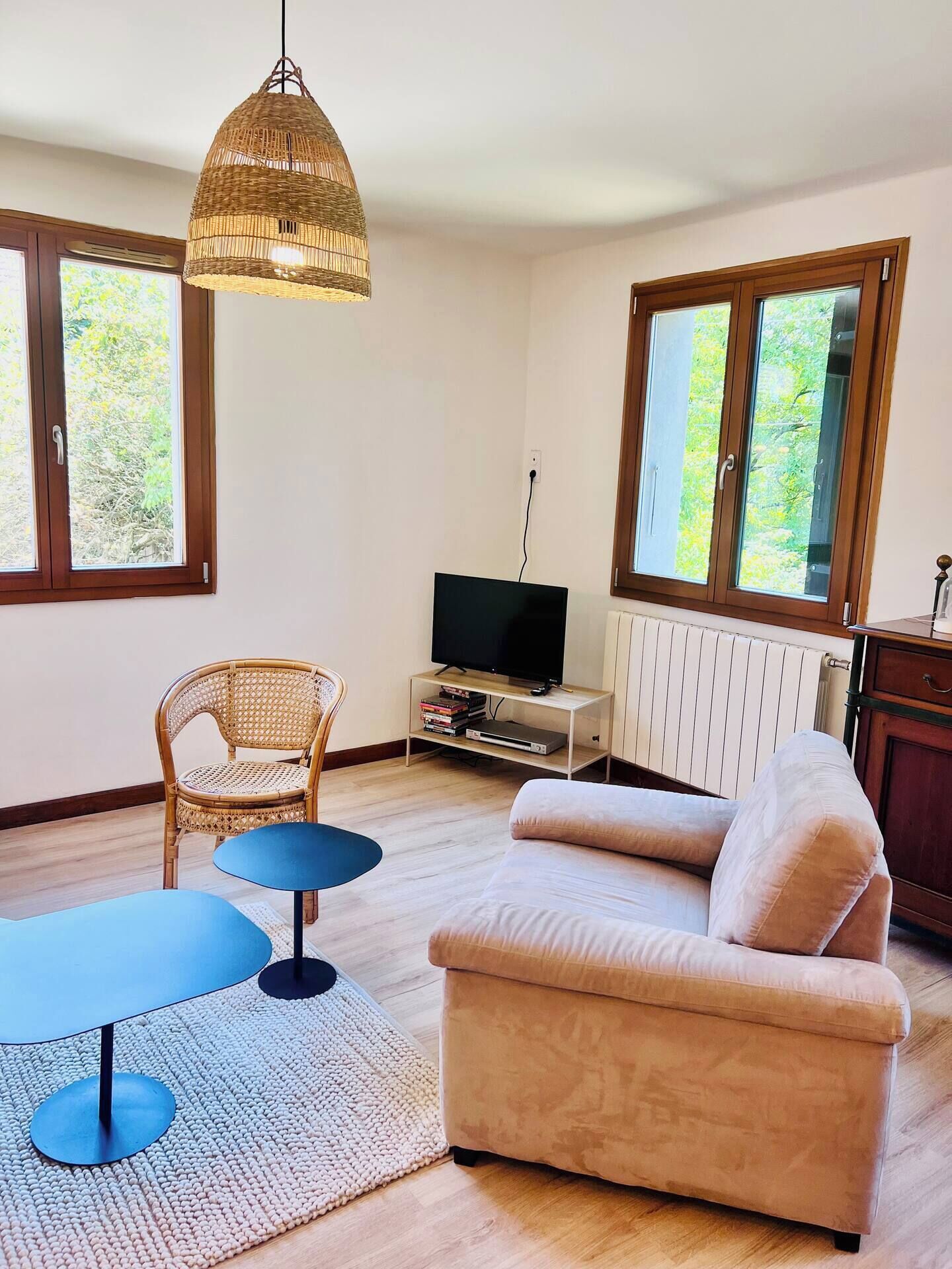Ein Wohnzimmer mit einer Couch, einem Fernseher, einem Korbstuhl und einer Hängelampe.