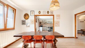 Un comedor con una mesa de madera y sillas naranjas, una araña y cuadros enmarcados en la pared.