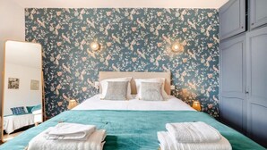 Una camera da letto con carta da parati floreale, un letto con lenzuola bianche, due comodini con lampade e un armadio blu.