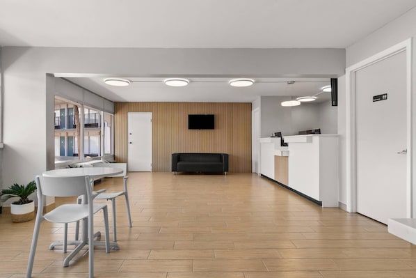 Uma área de recepção moderna com televisão de tela plana, balcão de atendimento e espaço de estar com mesa e cadeiras.