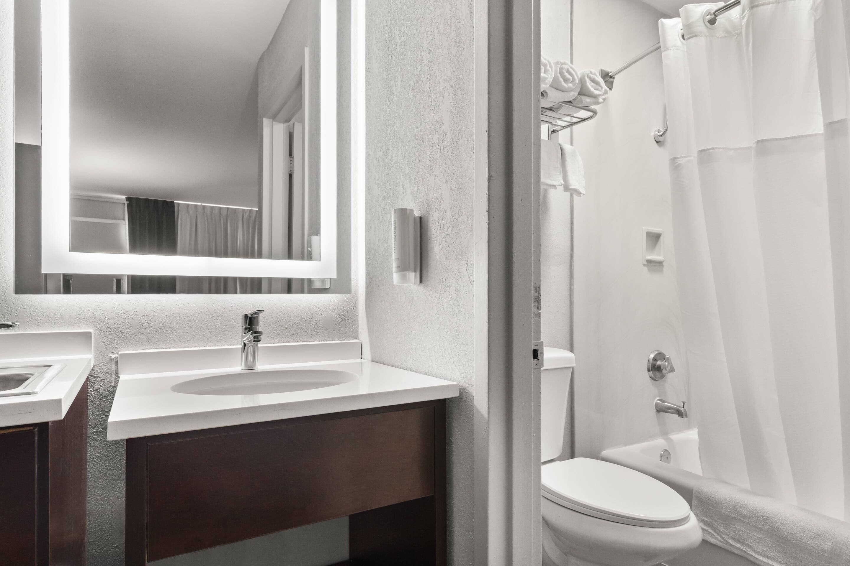 A modern bathroom with a large mirror, a sink, a toilet, and a shower area.