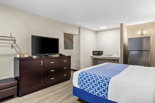 Habitación de hotel con cama, televisor, escritorio, microondas y refrigerador.