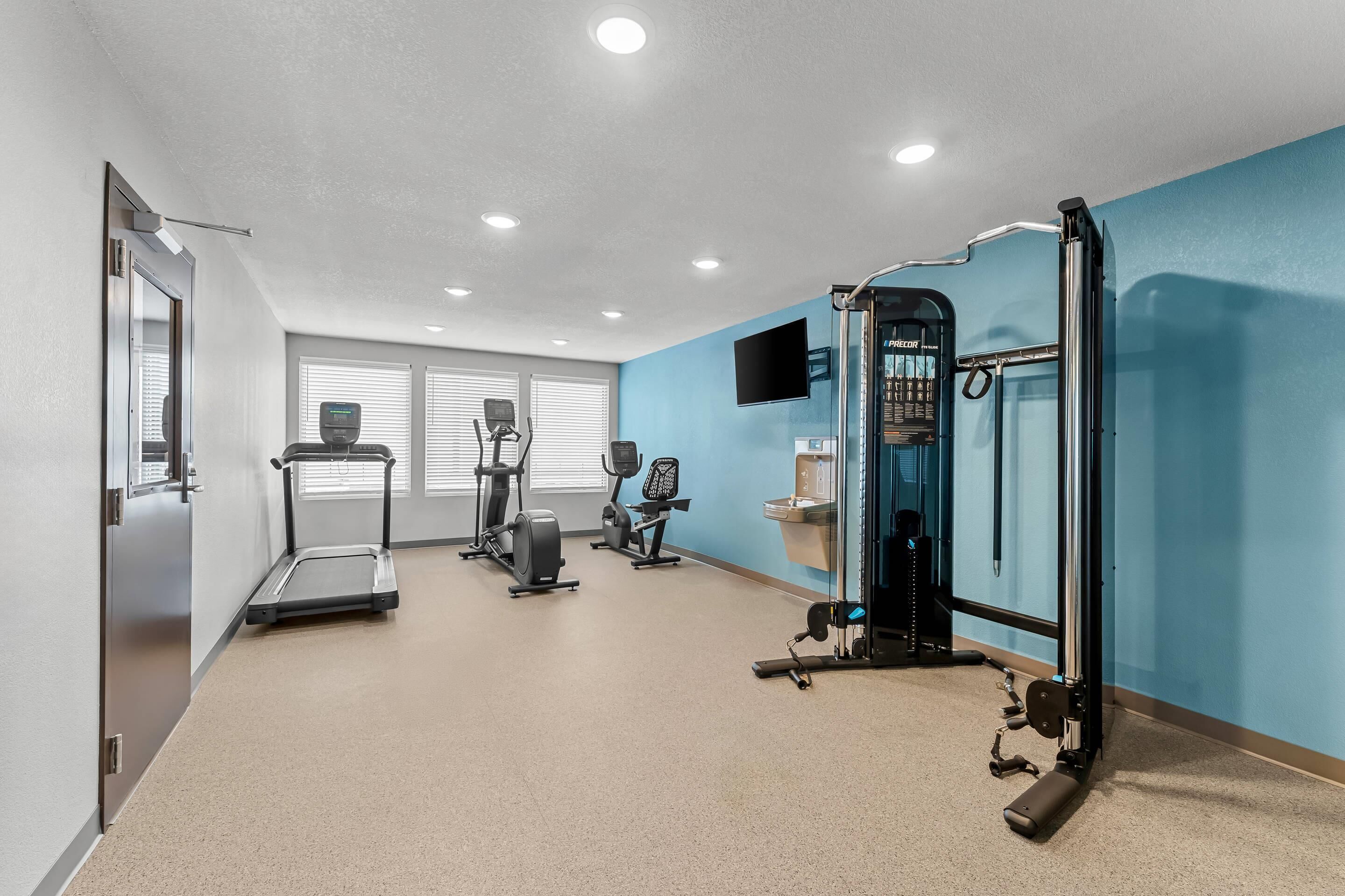 A fitness room with exercise equipment, a treadmill, and a wall-mounted TV.
