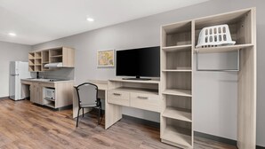 A modern kitchen with a built-in stove, a dining area with a chair, and a large TV on a wooden stand. - Woodspring Suites Wilmington Riverfront (Wilmington)