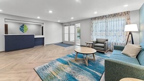 A modern hotel lobby with a reception desk, seating area, and a large window with curtains. - Woodspring Suites Wilmington Riverfront (Wilmington)
