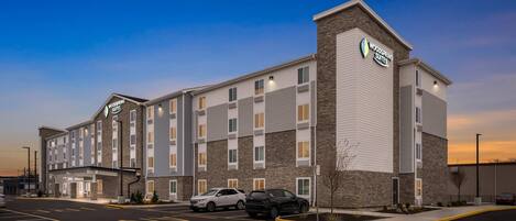 A modern hotel with a brick facade, multiple entry points, and a parking lot with several cars.