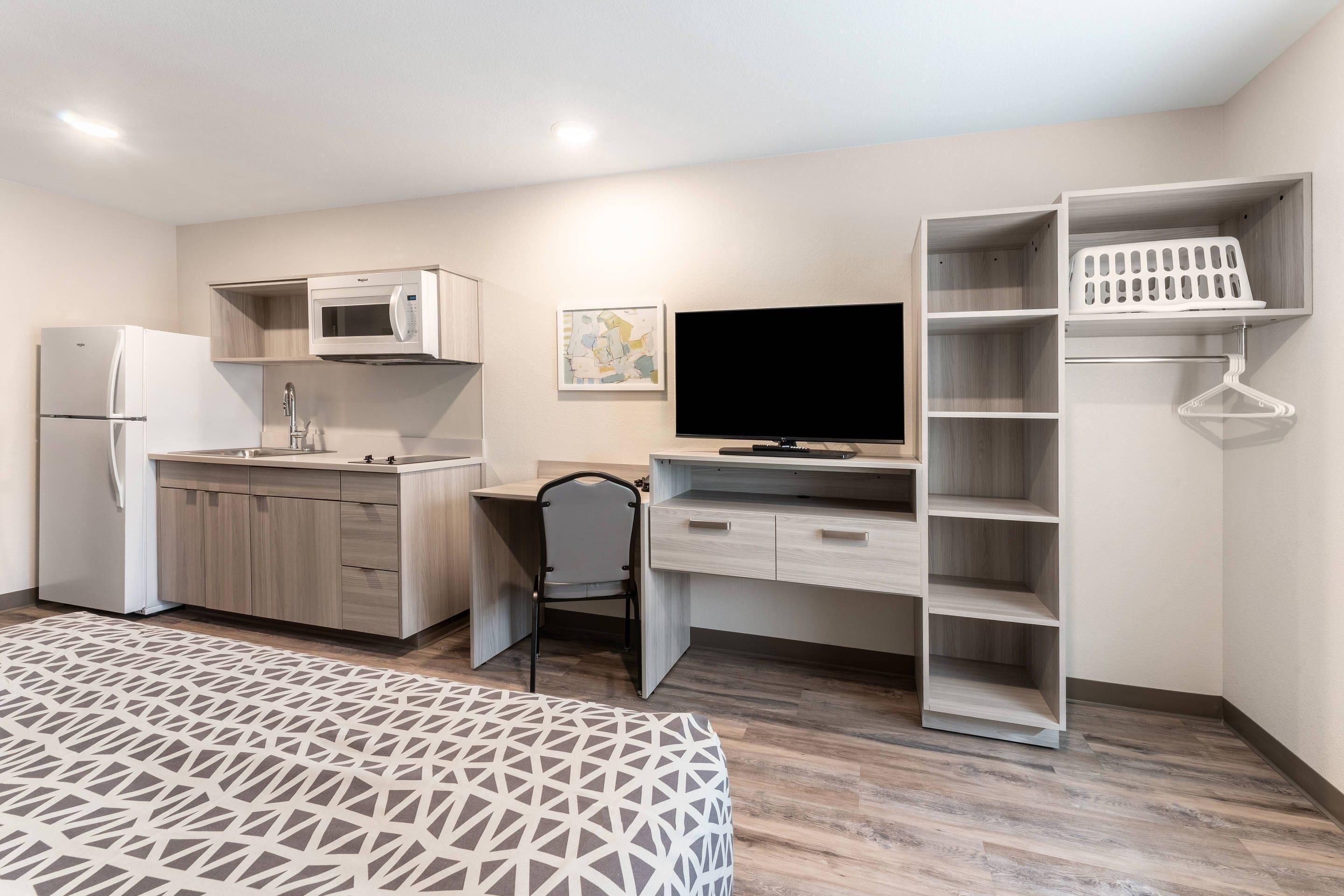 Une chambre compacte comprenant un coin cuisine, un téléviseur à écran plat, un bureau et un lit.