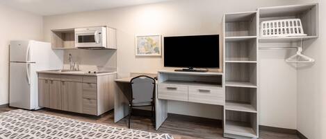 A compact room with a kitchenette, a flat-screen TV, a desk, and a bed.