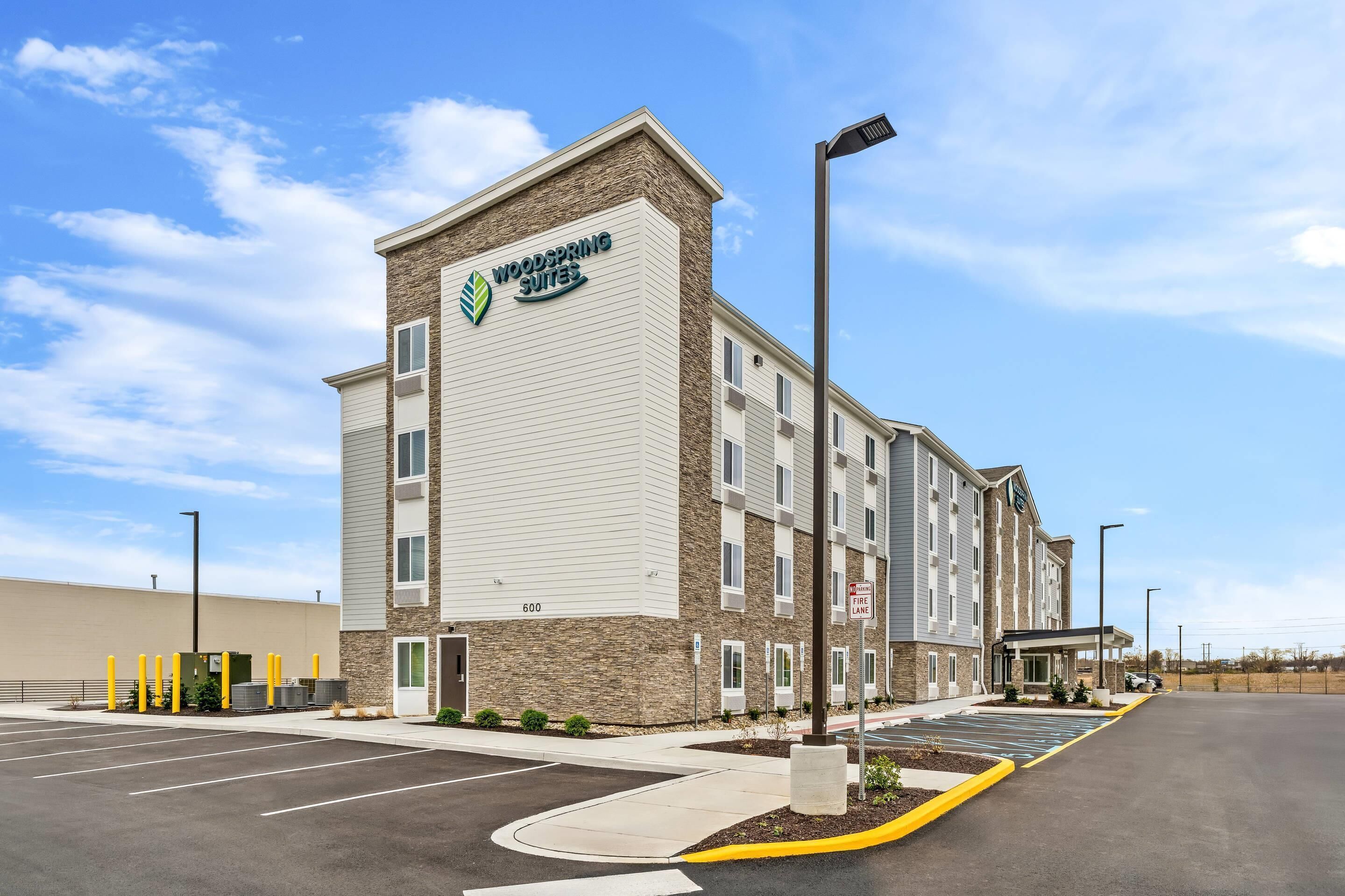 Un hôtel au design moderne, avec un logo bien visible sur la façade, un panneau indiquant la voie d’accès pour les véhicules d’urgence et un parking.
