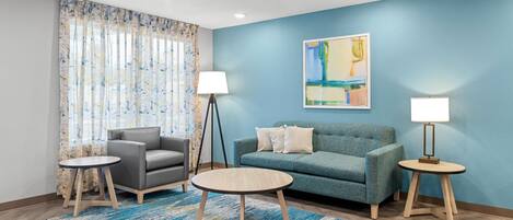 A modern living room with a blue accent wall, a grey sofa, a round coffee table, and two side tables with lamps.