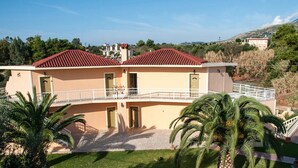 A two-story building with a red-tiled roof, a balcony with a white railing, and a car parked in front. - Makis Studios By La Skala Vista (Kefalonia)