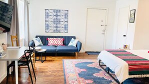 A room with a sofa, a bed, a dining table with chairs, a TV, and a patterned rug. - Texas Bluebonnet Décor Walkable Montrose Studio 14 Centralize Suite Studio! (Houston)