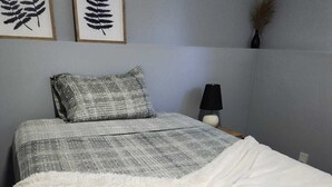 Et soveværelse med en seng, en pude, en sengetavle og to billeder af blade på væggen.