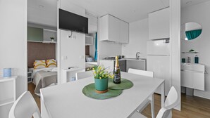 Ein modernes, helles Zimmer mit Esstisch, Stühlen, Fernseher, Küchenzeile und einem Bett mit Blick.