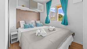 Ein modernes Schlafzimmer mit einem großen Bett, blaugrünen Vorhängen und Blick auf Grünflächen.