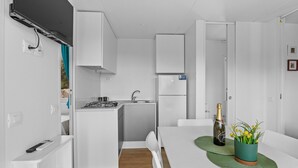 Eine moderne Küche mit weißen Schränken, einem eingebauten Herd und einem kleinen Kühlschrank. Ein Esstisch mit grüner Tischdecke und einer Champagnerflasche.