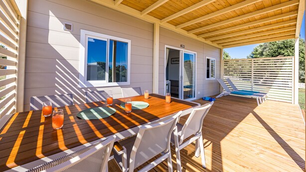 Une terrasse couverte avec une table et des chaises en bois, une piscine et une porte-fenêtre coulissante.