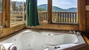 Una cabaña de madera con una bañera grande, un muro de piedra y vistas a montañas.