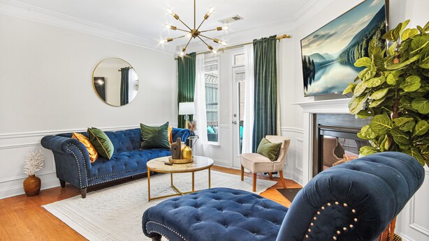 Een woonkamer met een blauwe bank, een ronde spiegel, een kroonluchter en een schilderij van een landschap.