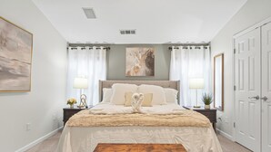 Een slaapkamer met een groot bed, twee nachtkastjes, een bankje, een kunstwerk aan de muur en een deur.