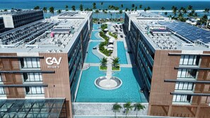A modern hotel with a central swimming pool, multiple floors, and a view of the ocean. - Gav Resort Piscinas Naturais by La Playa (Ipojuca)