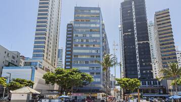 Paisagem urbana com edifícios altos, rua de areia e um pequeno quiosque.