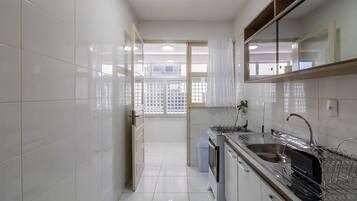 Uma cozinha moderna com azulejos brancos, eletrodomésticos de aço inoxidável e uma janela com vista para o exterior.
