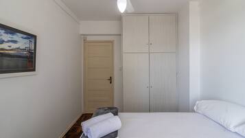 Quarto com cama, um banquinho com toalha, guarda-roupa e uma porta.