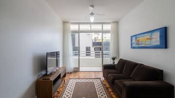 Sala de estar com sofá, televisão e ventoinha no teto.