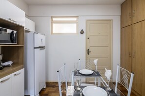 A compact kitchen with white appliances, a dining table set for two, and a small window above the door. - Apt. w/ Balcony & Sea View 360m Beach Ety0024 (Balneário Camboriú)